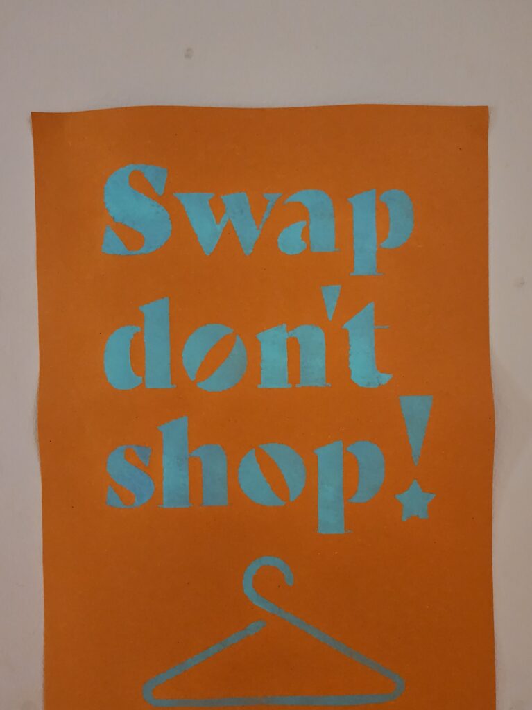 An orange Swap Don’t Shop! poster printed in turquoise with a coat hanger graphic