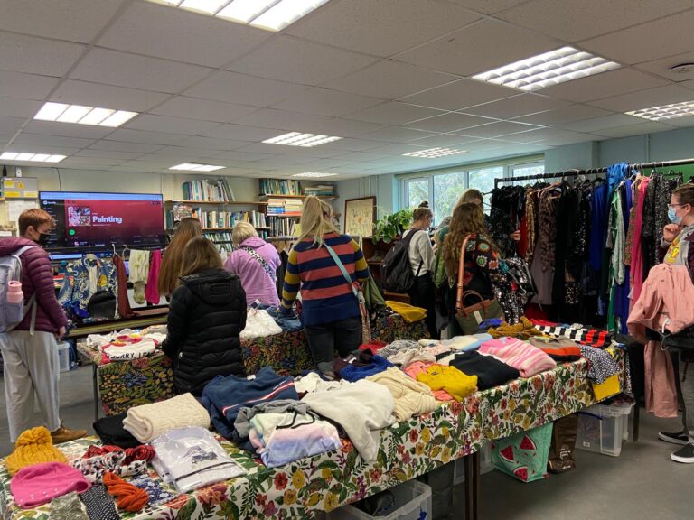 Swappers browsing tables of folded clothes and rails in a busy community room